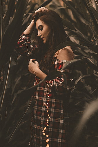 Woman in plaid dress standing in cornfield with fairy lights