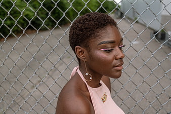 Portrait of stylish Black woman with pink eyeliner against fence