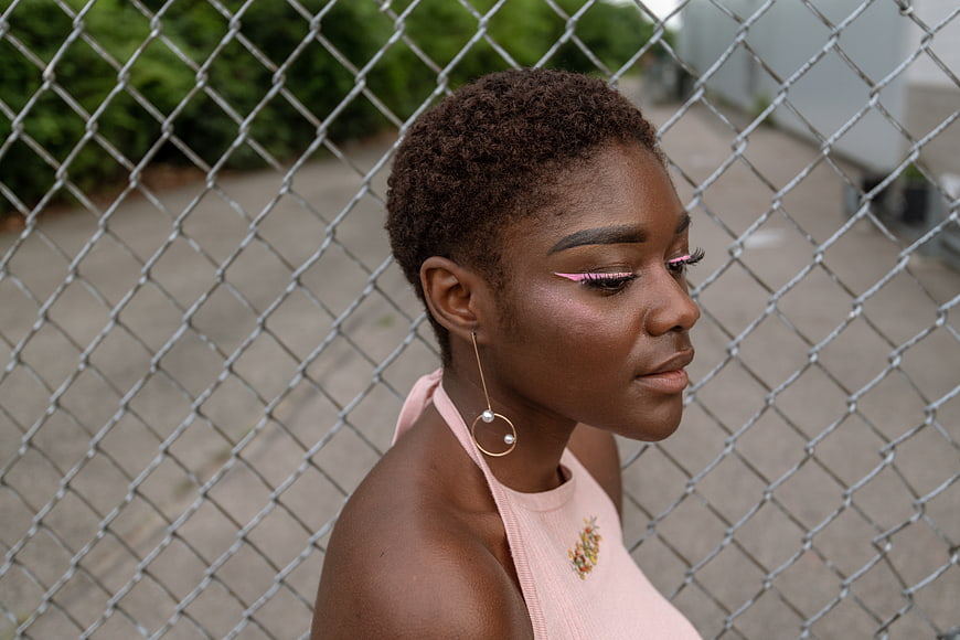 Portrait of stylish Black woman with pink eyeliner against fence