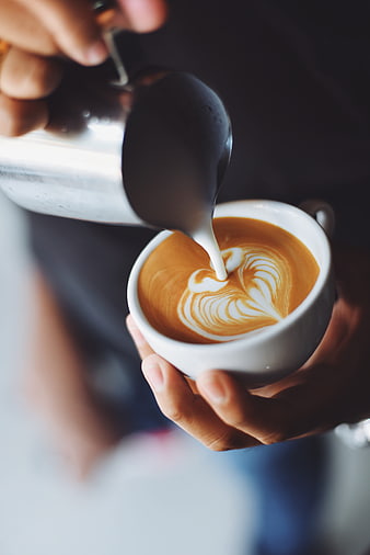 Barista pouring latte art into a white coffee cup