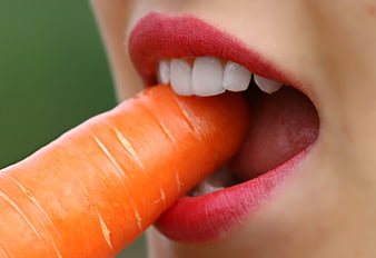 Close-up of woman biting fresh carrot with red lipstick