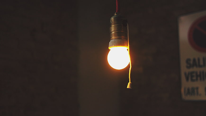 Glowing light bulb hanging in dark room with switch