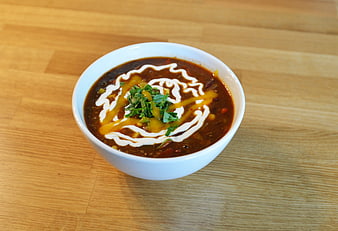 Bowl of chili soup with sour cream and cilantro on wood