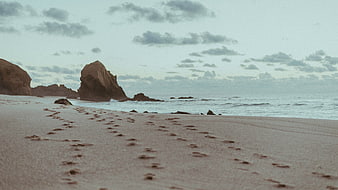 Footprints on Sandy Beach Leading to Ocean Rocks