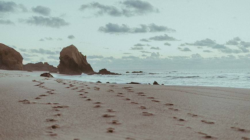 Footprints on Sandy Beach Leading to Ocean Rocks