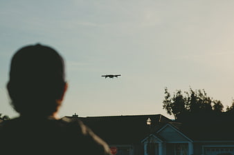 Silhouette of person flying drone over suburban neighborhood