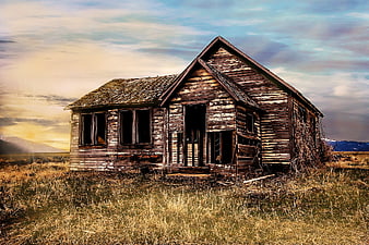 Abandoned wooden farmhouse in a field at sunset