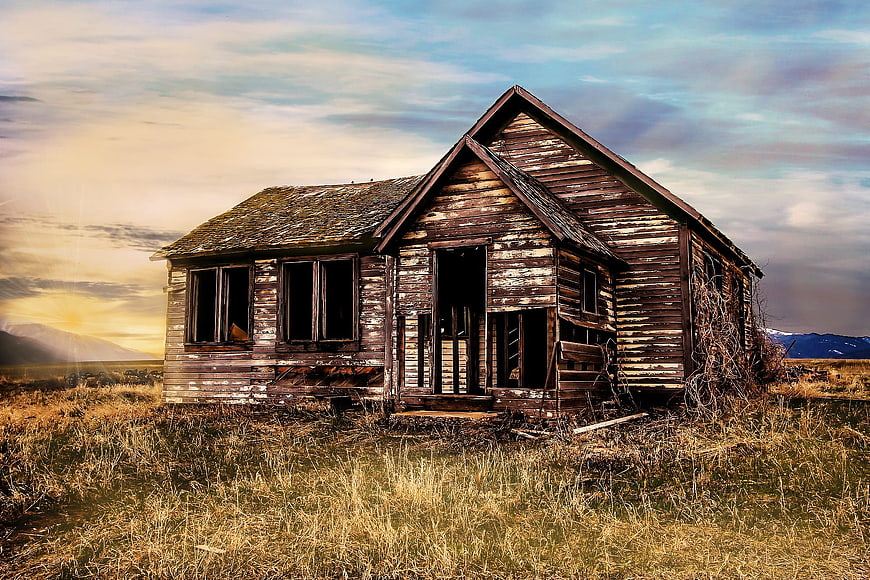 Abandoned wooden farmhouse in a field at sunset