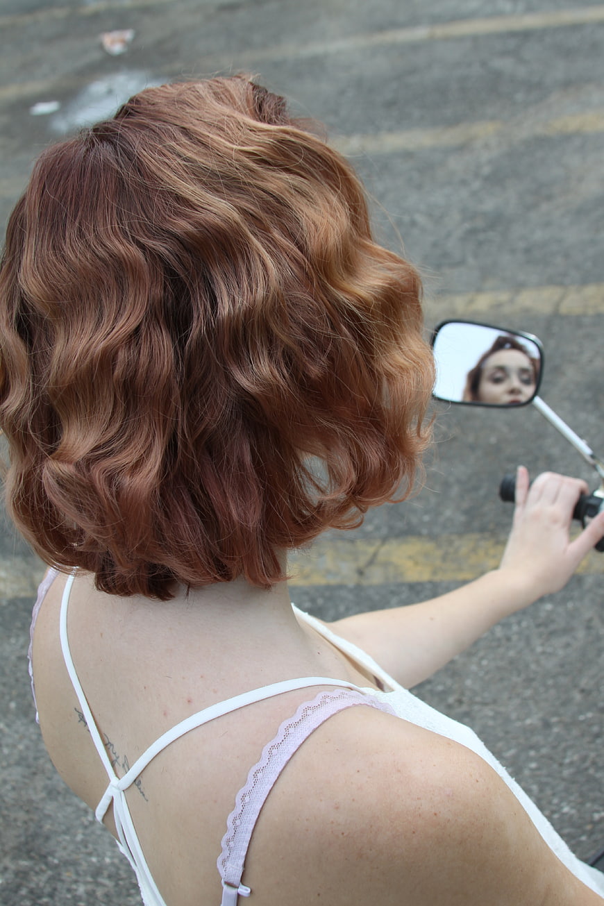 Woman with wavy hair looking in motorcycle mirror