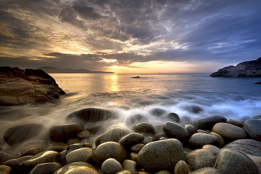 Dramatic Sunset Over Rocky Beach with Smooth Ocean Waves
