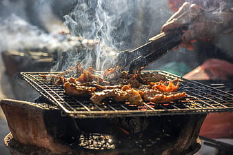 Close-up of sizzling meat grilling over charcoal with smoke