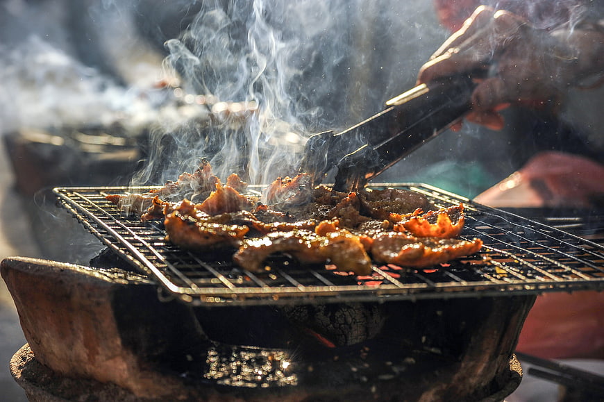 Close-up of sizzling meat grilling over charcoal with smoke