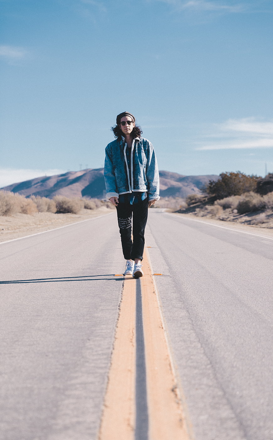 Man walking on desert highway with mountains