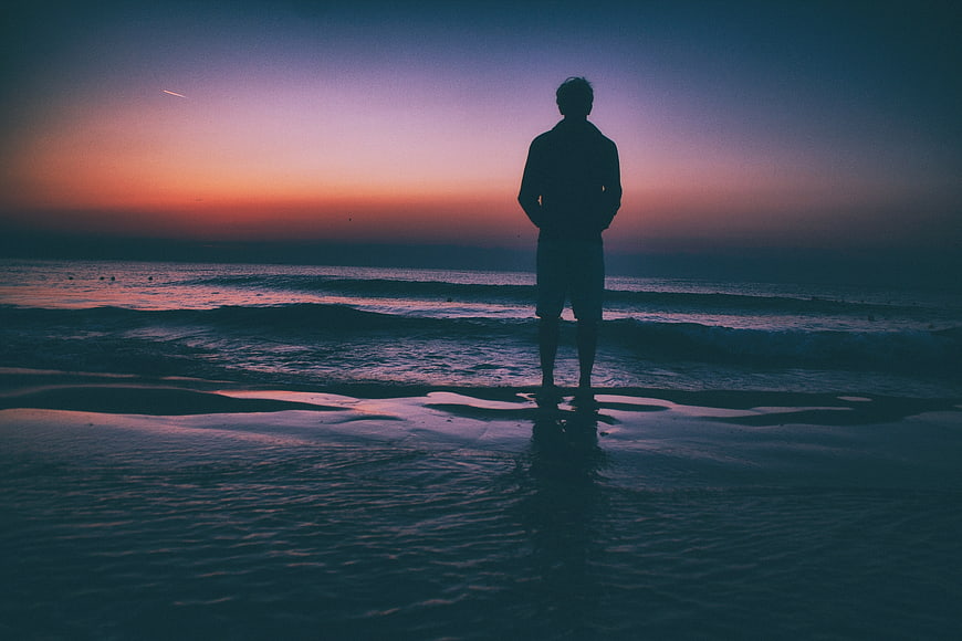 Silhouette of Man Standing on Beach at Sunset