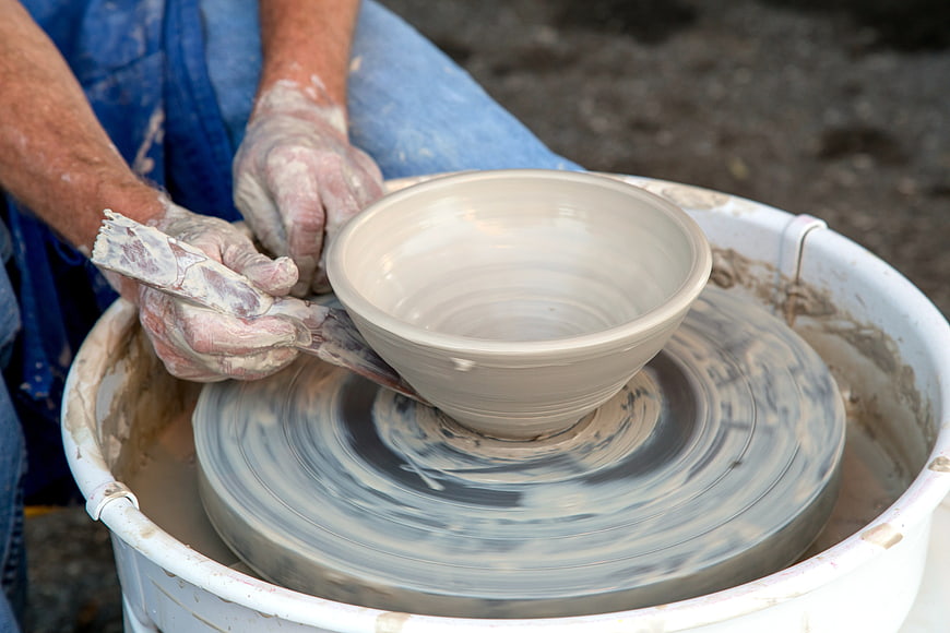 Potter shaping clay bowl on spinning wheel