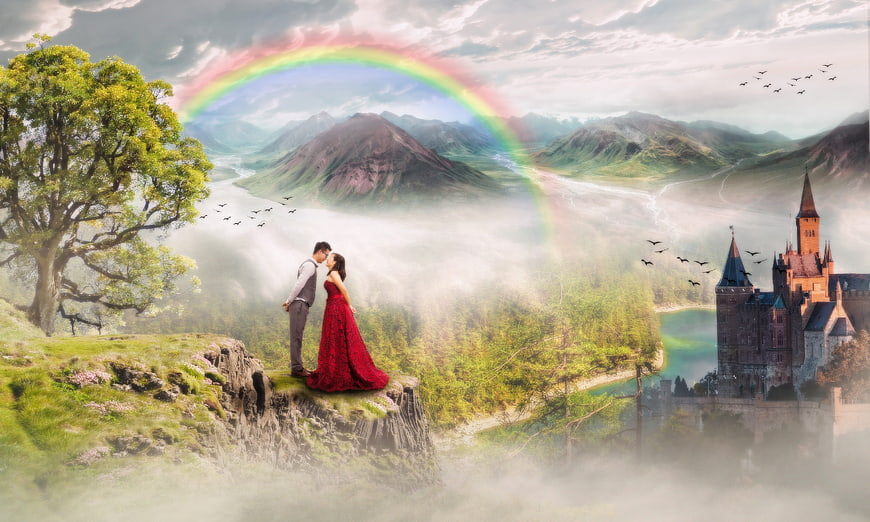 Romantic couple kissing on cliff with rainbow and castle