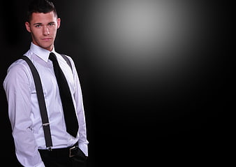Handsome young man in white shirt and suspenders on black background