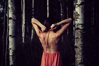 Woman tying orange dress in dark birch forest