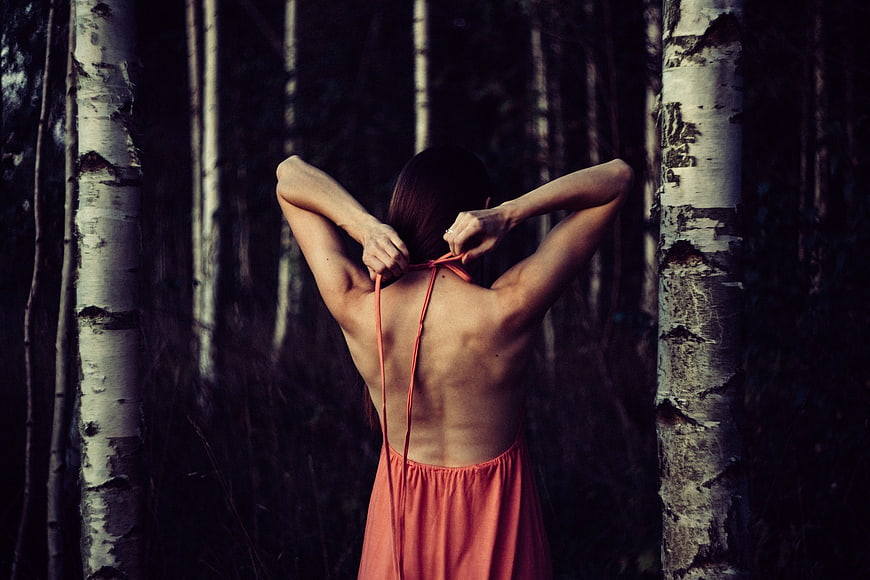 Woman tying orange dress in dark birch forest