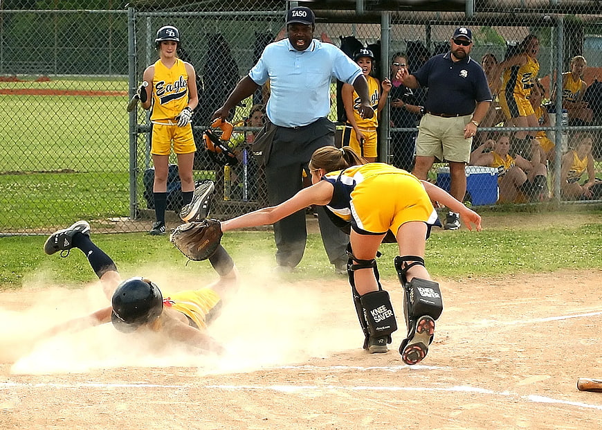 Softball player sliding into home plate with dust cloud