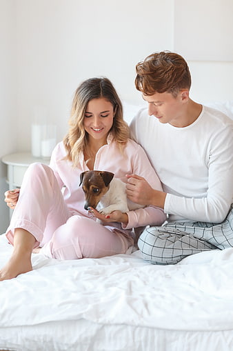 Happy young couple in pajamas playing with dog on bed