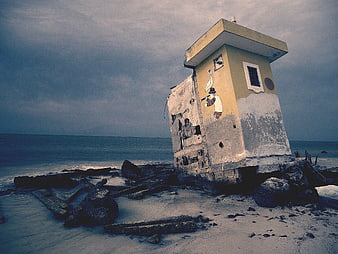 Abandoned yellow lifeguard tower on rocky beach with mural