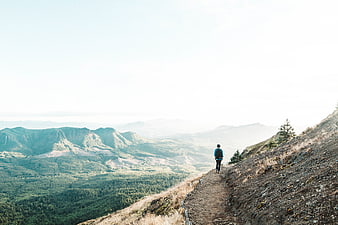 Hiker walking on mountain ridge trail with forest valley view