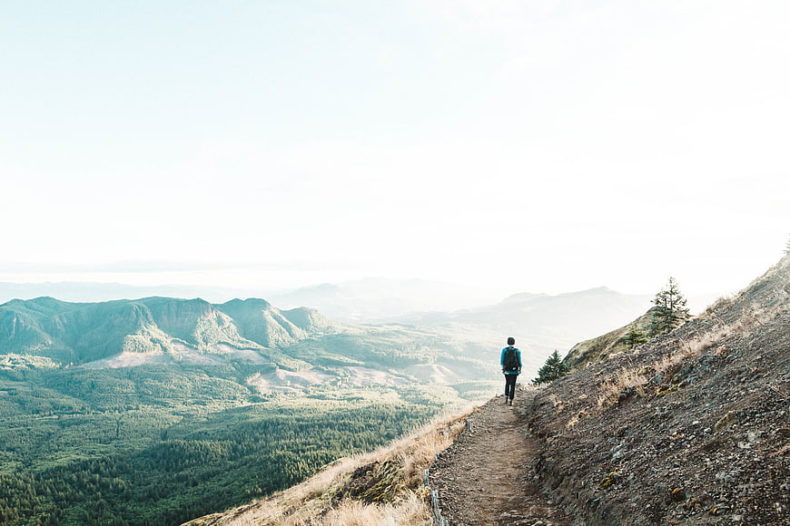 Hiker walking on mountain ridge trail with forest valley view