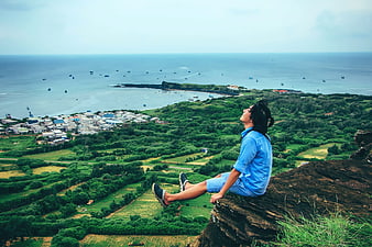Man sitting on cliff overlooking coastal village and ocean