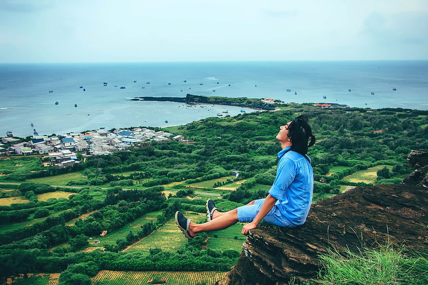Man sitting on cliff overlooking coastal village and ocean