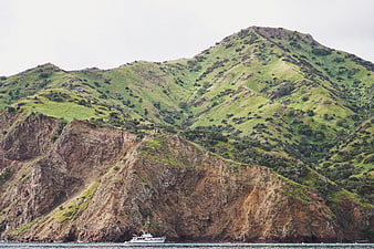 Green mountain cliffs overlooking ocean with small boat