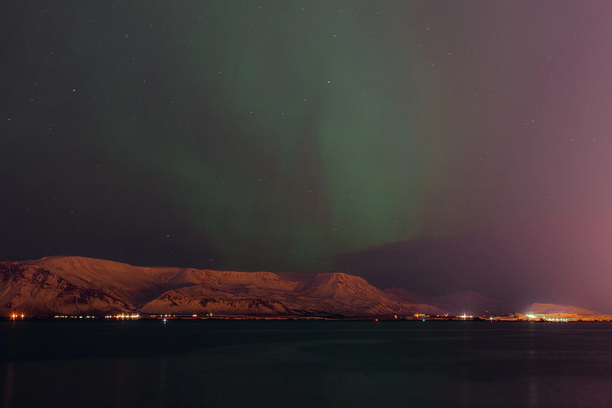 Aurora Borealis over Snowy Mountains and Coastal Town