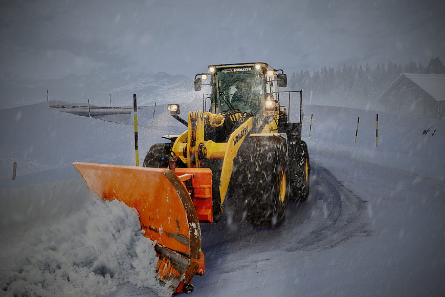 Yellow wheel loader clearing snow on a mountain road during a blizzard
