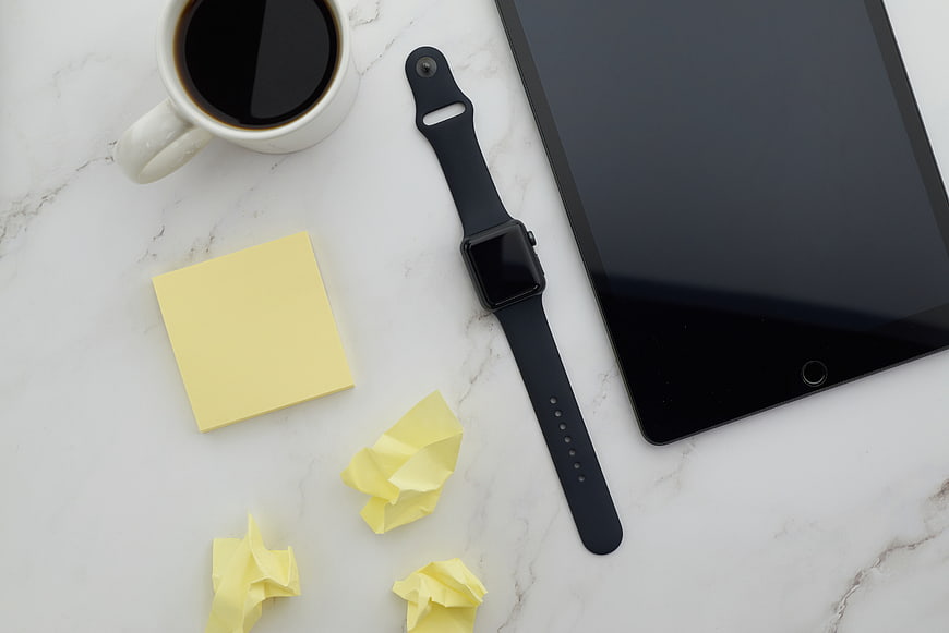Flat lay of workspace with tablet, smartwatch, coffee, and sticky notes