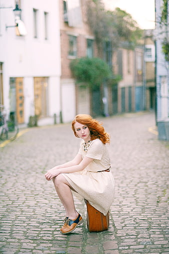 Redhead woman sitting on suitcase in cobblestone street