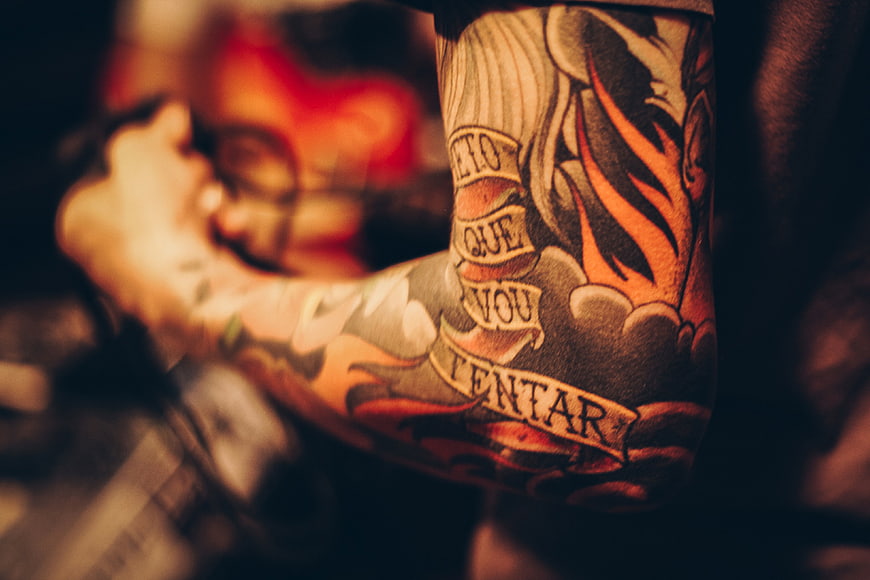 Close-up of tattooed arm with Portuguese phrase and flames