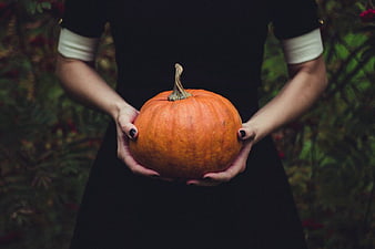 Woman in Black Dress Holding Orange Pumpkin