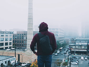 Man in Hoodie Looking at Foggy City Skyline