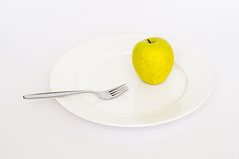 Yellow apple and fork on white plate for healthy diet concept