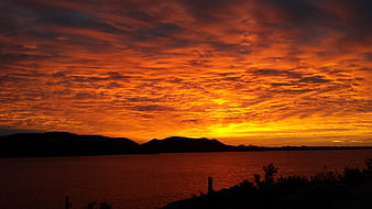 Dramatic fiery orange sunset over silhouetted mountains and water