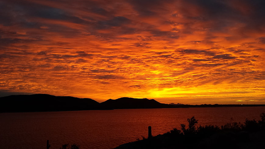 Dramatic fiery orange sunset over silhouetted mountains and water