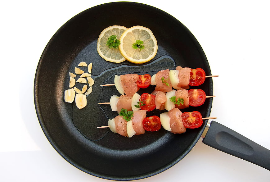 Raw chicken skewers with vegetables in frying pan
