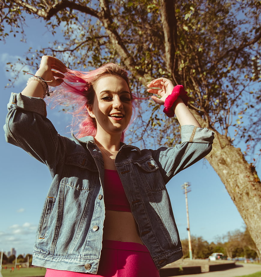 Happy young woman with pink hair playing outdoors in denim jacket