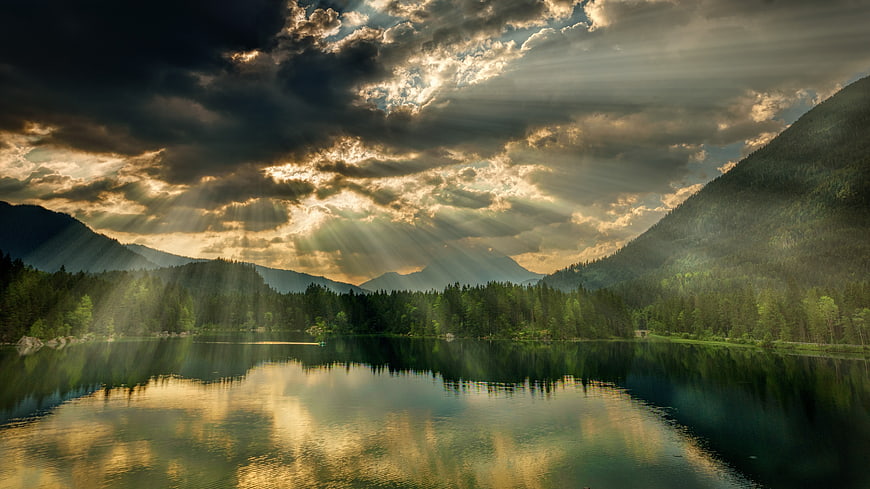 Dramatic Sun Rays Over Mountain Lake with Forest Reflection