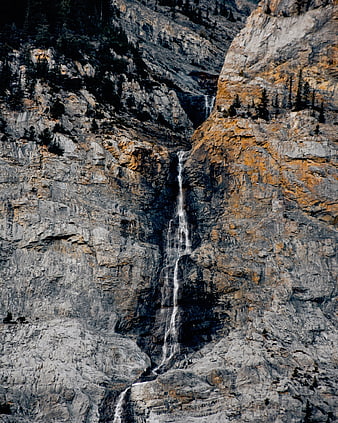 Tall waterfall cascading down rugged mountain cliff face