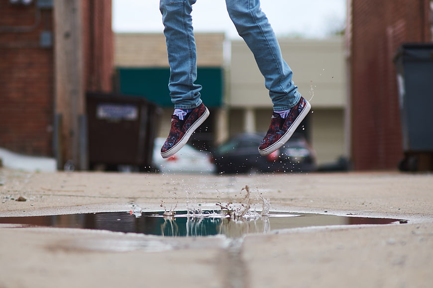 Man jumping over puddle in jeans and sneakers