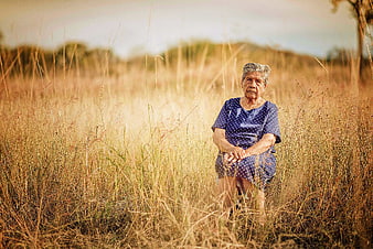 Elderly woman sitting in golden dry grass field