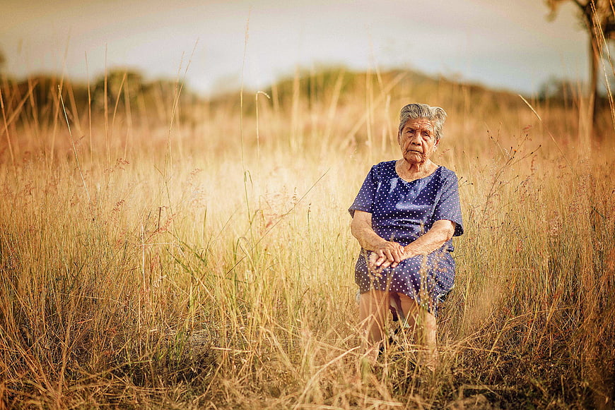 Elderly woman sitting in golden dry grass field