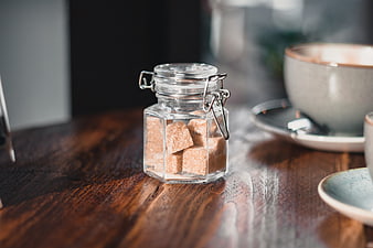 Glass jar of brown sugar cubes on wooden table with coffee