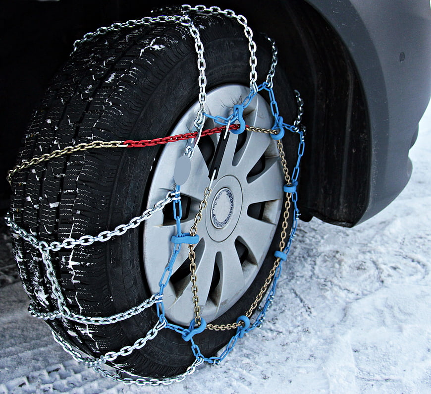 Car tire with snow chains installed on snowy winter road